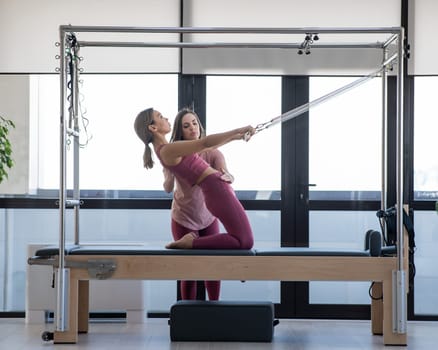 Asian woman doing pilates with trainer on cadillac reformer