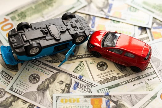 concept of car accident loss and damage. two model cars on the heap of us hundred dollars. . High quality photo