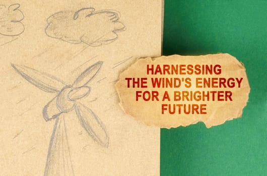 Alternative energy concept. On a green surface there is a drawing with a wind generator and a cardboard with the inscription - Harnessing the wind's energy for a brighter future