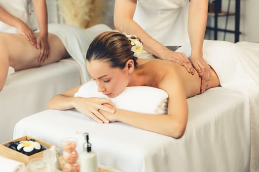 Caucasian couple customer enjoying relaxing anti-stress spa massage and pampering with beauty skin recreation leisure in day light ambient salon spa at luxury resort or hotel. Quiescent