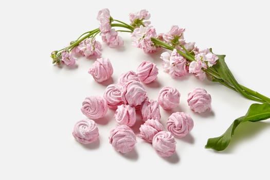 Velvety natural berry pink marshmallow swirls accompanied by fragrant spring flowers, showcased on white background, emphasizing airy texture and purity. Healthy dessert concept