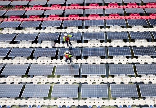 Wide shot of top view two technician workers stand and check to maintenance solar cell panels over the water reservoir as solar farm factory in concept of green energy for good environment.