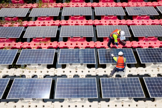 Top view of two technician workers check and maintenance solar cell panels over the water reservoir as solar farm factory in concept of green energy for good environment.