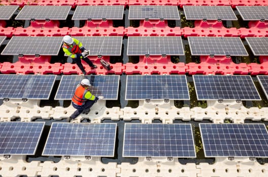 Close up and top side view of two technician workers check and maintenance solar cell panel over the water reservoir as solar farm factory.