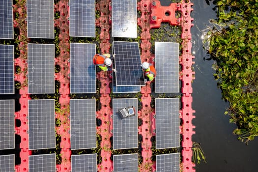 Close up and top view of two technician workers set up or install solar cell panel over the water reservoir as solar farm factory in concept of green energy for good environment.