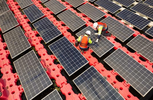 Close up and top view of two technician workers check and maintenance solar cell panel over the water reservoir as solar farm factory in concept of green energy for good environment.