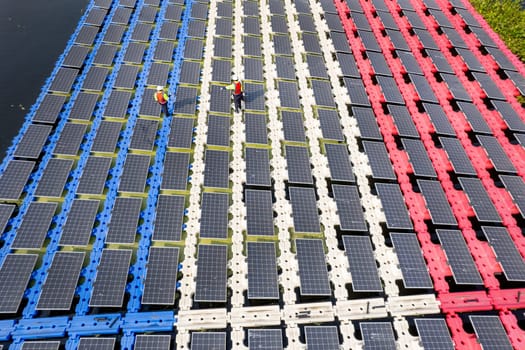 Wide shot of aeroview or top view of two technician workers walk along the solar panel system over water resirvoir for green ecosystem energy for good environment.