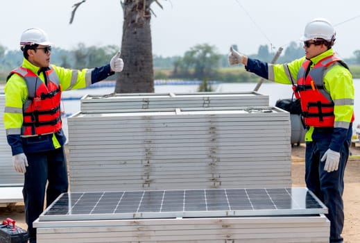 Two Asian technician worker stand beside solar cell panel and show thumbs up to each other in concept of green energy system and success of work.