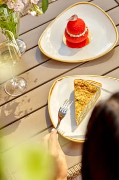 Delightful al fresco lunch featuring slice of savory cheese and spinach quiche, crunchy red Choux au Craquelin with cream and glass of white wine on sunny day