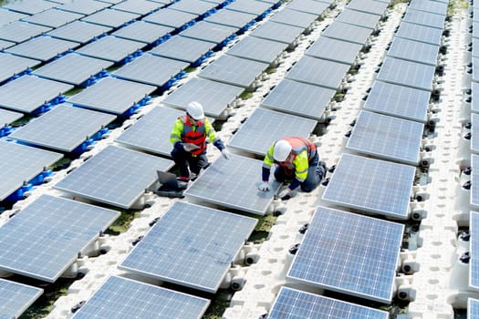 Two professional technician workers with safety uniform work with solar cell panels system to check and maintenance over water reservoir in concept of green energy environment.