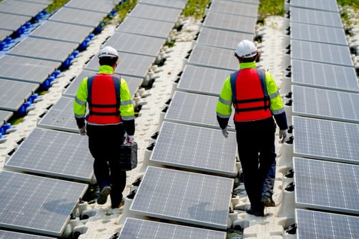 Back of professional with safety uniform walk on footpath along row of solar cell panels in workplace concept of green energy power plant for good environment.