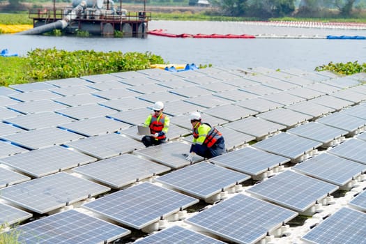 Wide shot of professional technician workers sit and work with solar cell panel also use laptop over the water reservoir.