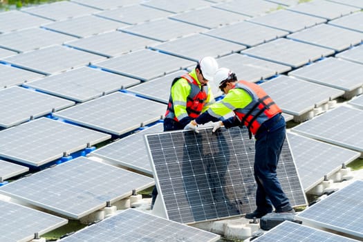 Two Asian technician workers stand and help to install or set up solar panels over water reservoir in the plant for green energy factory system workplace.
