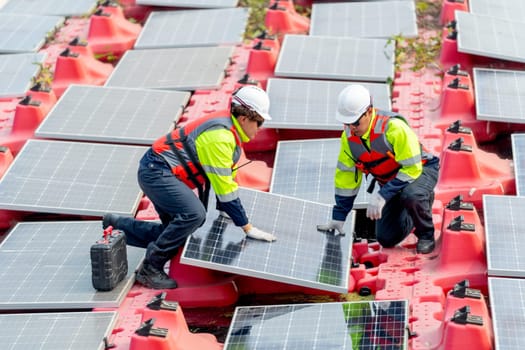 Side view of two professional technician workers hold solar cell panels with touch to check problem during installation or set up to the system and they work over water reservoir area.