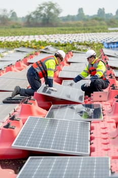 Vertical image of professional technician worker use laptop to work with other co-worker touch to check and maintenance solar cell panel in workplace over water reservoir.