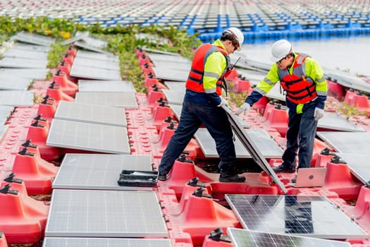 Side view of two professional technician workers hold solar cell panels with check problem during installation or set up to the system and they work over water reservoir area.