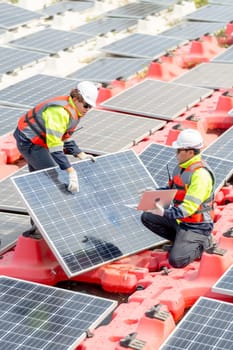 Vertical image of two technician workers help to check and maintenance solar cell panels that set up over area of water reservoir.