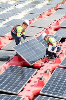 Vertical image of two technician workers help to installation or set up solar cell panels that base over area of water reservoir.