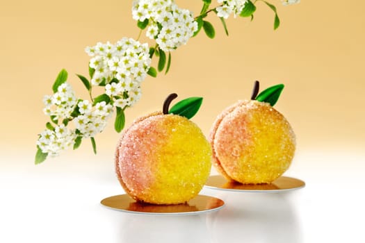 Two peach-shaped cakes with sugar sprinkles, presented on golden plates against warm background with tree branch blooming with white flowers