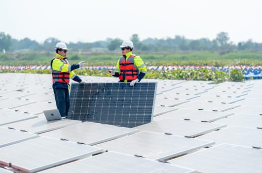 Two professional technician workers stand and hold solar cell panel also discuss together in area of network of base over area of water reservoir.