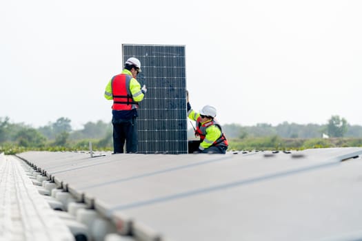 Professional technician worker sit and hold solar cell panel to check and maintenance also work with co-worker stand in front of the panel.