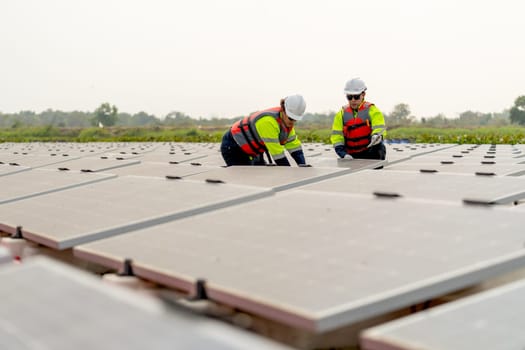 Wide shot of two technician workers sit and work on process of maintenance solar cell panel network system in concept of green energy power.