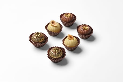 Elegant artisan chocolates decorated with hazelnuts, caramel crumbs and golden pearls, on white background
