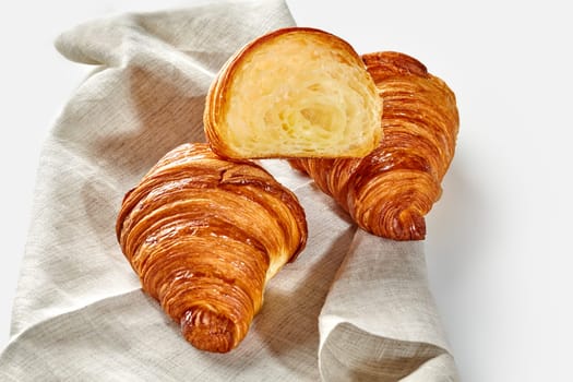 Traditional freshly baked French croissants with perfectly flaky texture, captured in rustic setting on woven linen cloth