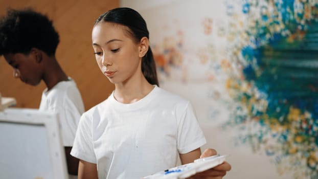 Multicultural student paint the canvas together in art lesson with colorful stained wall. Closeup of african boy and caucasian girl drawing picture or doing creative activity together. Edification.