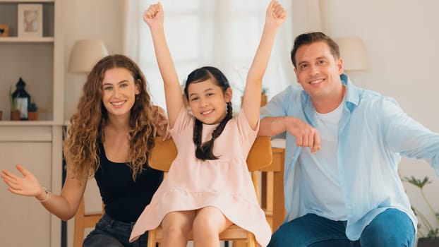 Happy family portrait with lovely little girl smile and looking at camera, lovely and cheerful parent and their daughter sitting together in living room at home with warm daylight. Panorama Synchronos