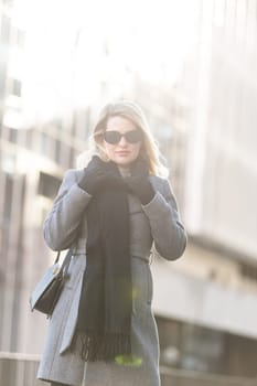 Young beautiful blonde girl in coat with a black bag walks through the winter and spring city. High quality photo