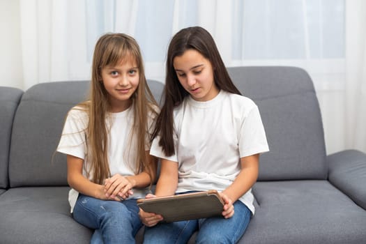 Cute little girl and older sister playing together smiling and having bonding time using a laptop on couch at home. Happy family Siblings relationship and digital technology lifestyle concept. High quality photo