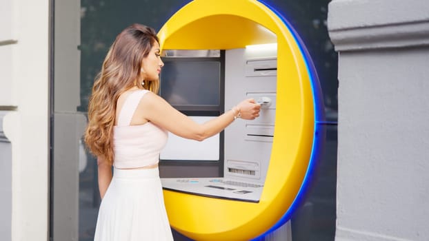 Young woman in white dress withdrawing money from the ATM in the street