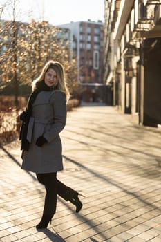 Beautiful young stylish blonde woman wearing long coat walking through the city streets. Trendy casual outfit. Street fashion. . High quality photo