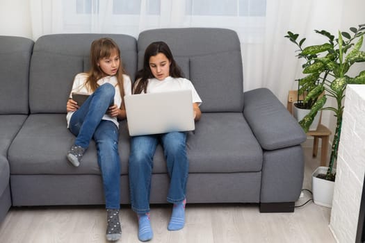 Cute little girl and older sister playing together smiling and having bonding time using a laptop on couch at home. Happy family Siblings relationship and digital technology lifestyle concept. High quality photo