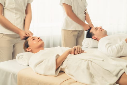 Caucasian couple enjoying relaxing anti-stress head massage and pampering facial beauty skin recreation leisure in dayspa modern light ambient at luxury resort or hotel spa salon. Quiescent