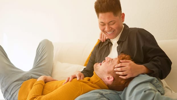 Multiethnic gay couple in love smiling together lying on the sofa