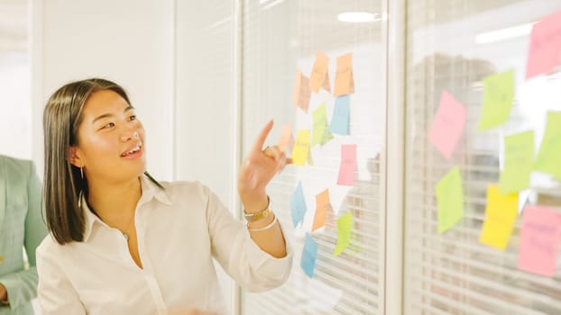 Chinese woman pointing a post-it to present ideas in a meeting