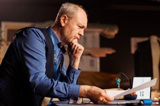 Dressmaker dissecting ideas, unable to come up with inspiration for upcoming fashion runway show project. Senior tailor overthinking in atelier shop workspace, looking for perfect sartorial outfit