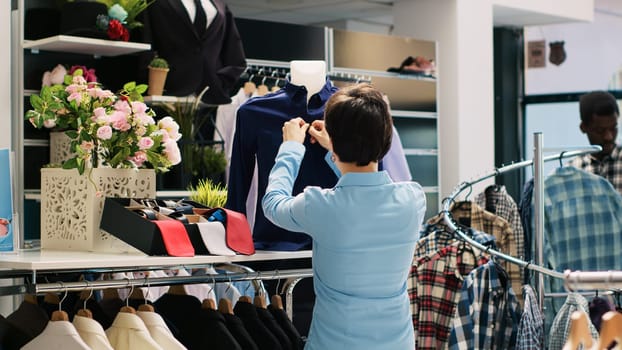 Employee working at boutique opening, putting formal wear on mannequin. Shopping centre manager arranging fashionable merchandise and accessories, new fashion collection in clothing store