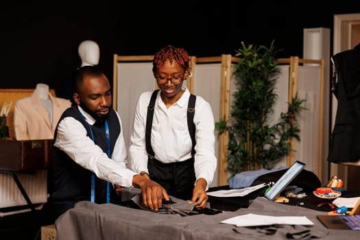 Precise suitmaking process in tailoring studio by african american fashion designers cutting sartorial textile material before making handmade costume. Couturiers working on customer comission