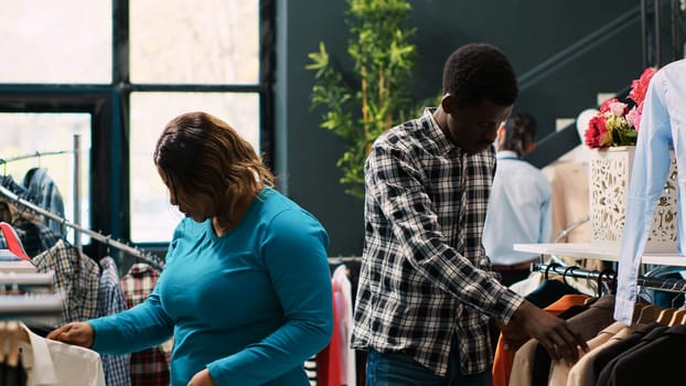 African american clients checking new fashion collection, shopping for casual wear in modern boutique. Cheerful couple analyzing clothes material, buying stylish merchandise. Fashion concept