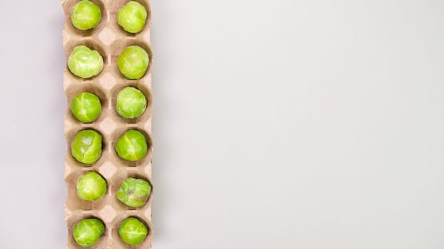 Raw organic Brussel sprouts in brown egg container on grey background, top view. Flat lay, overhead, from above. Copy space