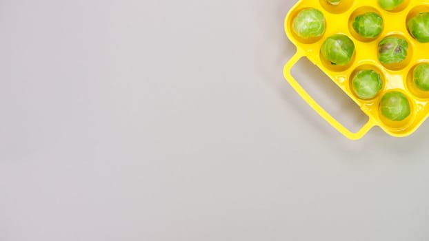 Raw organic Brussel sprouts in yellow container on grey background, top view. Flat lay, overhead, from above. Copy space