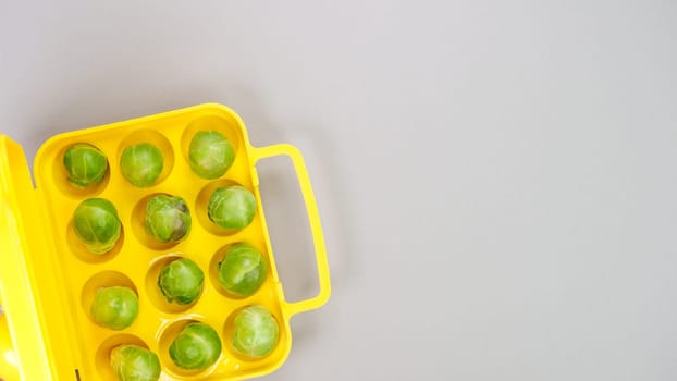 Raw organic Brussel sprouts in yellow container on grey background, top view. Flat lay, overhead, from above. Copy space