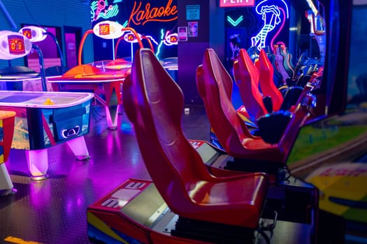 Row of racing arcade machines inside a neon-lit shopping mall, complemented by various gaming machines in an illuminated arcade. Entertainment concept.