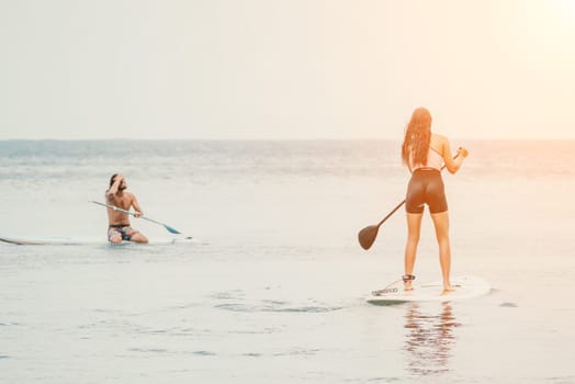 Sea woman and man on sup. Silhouette of happy young woman and man, surfing on SUP board, confident paddling through water surface. Idyllic sunset. Active lifestyle at sea or river