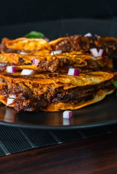 3 crispy, juicy beef birria tacos stacked on a black plate. Appetizing layout of amazing Mexican food in Tijuana, Mexico.