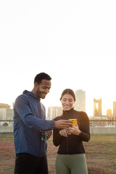 Young multiracial couple checking fitness statistics on mobile phone app after working out together outdoors. Couple running looking phone. Vertical image. Fitness and technology.