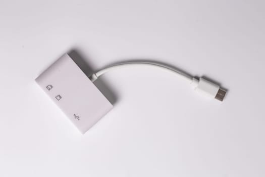 A white charger with two USB ports and an SD card reader is placed on a white surface. It serves as an electronics accessory and communication device for connecting multiple devices